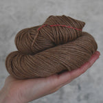 A skein of brown yarn held in a hand against a neutral background