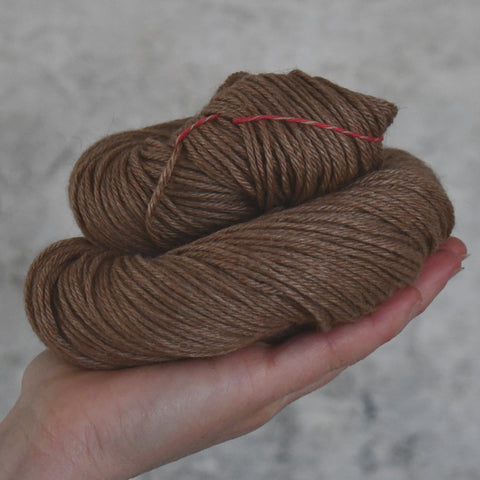 A skein of brown yarn held in a hand against a neutral background