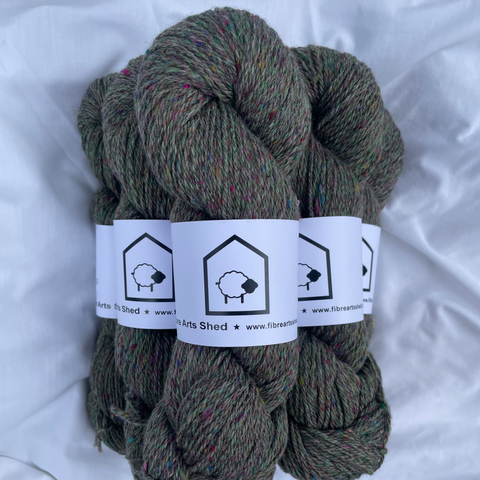 Three skeins of green yarn with labels on a white fabric background