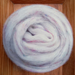 Spool of white roving with pink and blue speckles on a wooden surface