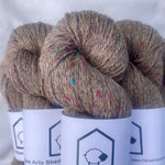 Three skeins of brown yarn with speckles on white fabric, labeled 'Fibre Arts Shed'.